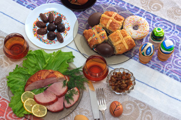 Traditional easter dinner set with sliced meat with lemon and herbs, handmade colored eggs, chocolates, raisins, easter cake and glasses of juice on colorful tablecloth