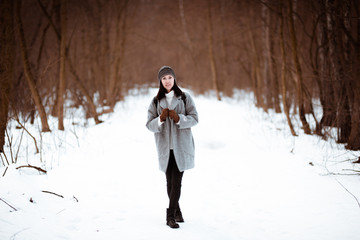 Portrait of a happy beautiful girl with brown hair in  winter forest.Attractive brunette woman dressed in a hipster style with black stylish leather backpack wearing grey coat and white pullover.