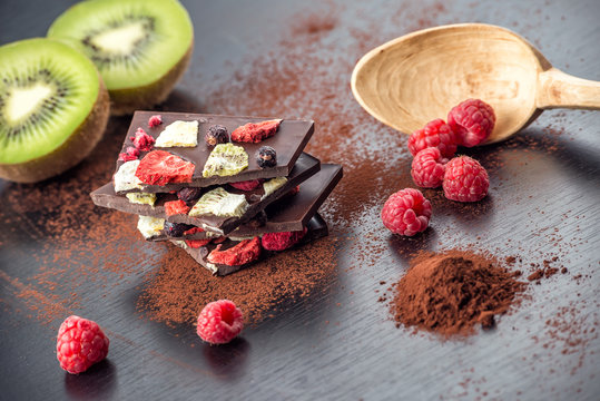 Sweet chocolate slices with fruits, cocoa powder and wooden spoon. sweet dessert on black background. image for patisserie