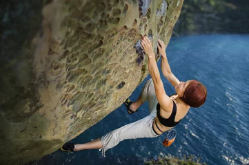 Foto op Canvas Young athletic female rock-climber on large boulder, hanging on one hand and holding hand in magnesium bag. Looking at the camera. Summer time © anatoliy_gleb