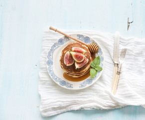 Pancake tower with fresh figs and honey on a rustic plate. Light blue  background