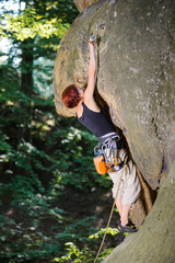 Young female lead climber climbing rocky wall and clipping carbine on her route. Summer time.