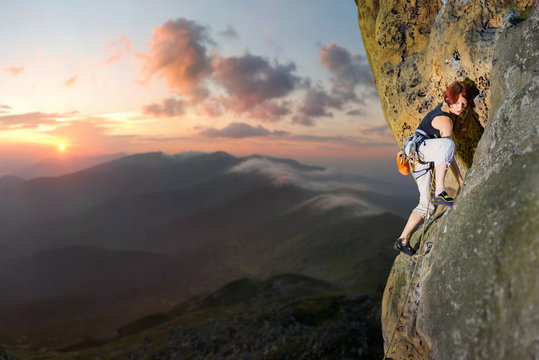 Young female rock climber climbing challenging route on rocky wall against scenic sunset background. Summer time.