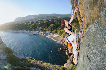 Athletic woman climbing an overhanging cliff against the scenic sea coast background. Summer time.