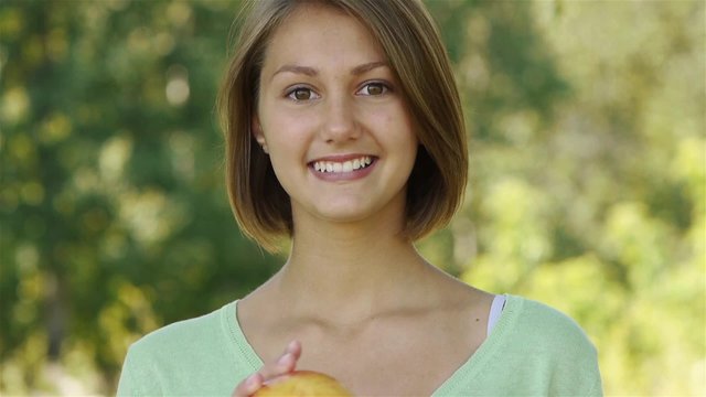 Portrait of smiling beautiful young woman close up with apple, against background of summer green park.