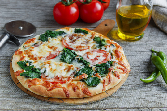 pizza with spinach tomato and cheese on a wooden surface