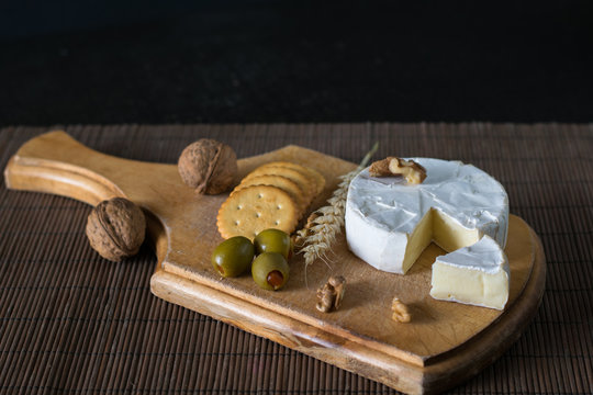 camembert and blue cheese with green olives and crackers on the wooden board as a perfect appetizer