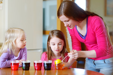 Young mother and her two little daughters painting colorful Easter eggs