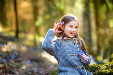 Adorable little girl picking the first flowers of spring in the woods