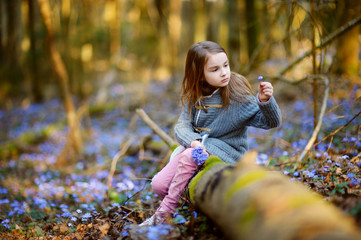 Adorable little girl picking the first flowers of spring in the woods