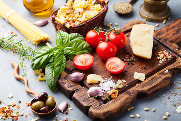 Italian food background with vine tomatoes, basil, spaghetti, olives Ingredients on stone table Copy space