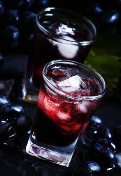 Cold juice of black grapes with ice on a dark background, select