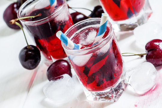 Cold cherry juice with ice on a white wooden background, selecti