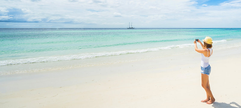 Female tourist taking photo of beautiful island beach on smartphone. Banner edition.