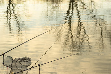 Reflection of trees in water with floating fishnet folding fish mesh basket and fishing rod