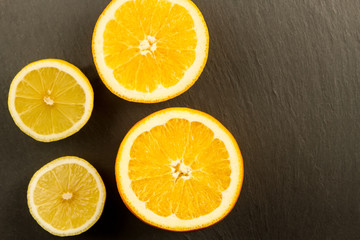 Fototapeta na wymiar cut a ripe lemon and orange on a black stone background