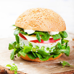 Vegetarian burger with egg and pea patty, fresh salad on a cutting wooden board
