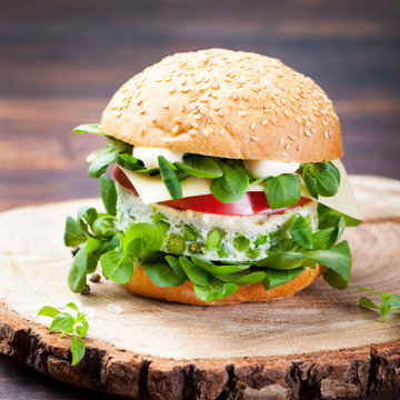 Vegetarian burger with egg and pea patty, fresh salad on a cutting wooden board