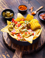 Nachos with melted cheese sauce, salsa and corn cobs in bowl on brown wooden background