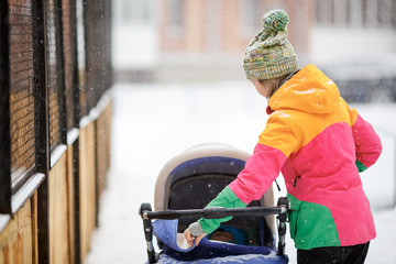 Mom and baby in stroller on walk, snowy winter weather. Snowfall, blizzard, outdoor.