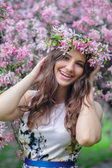 beautiful smiling woman with a wreath in the blossoming spring garden