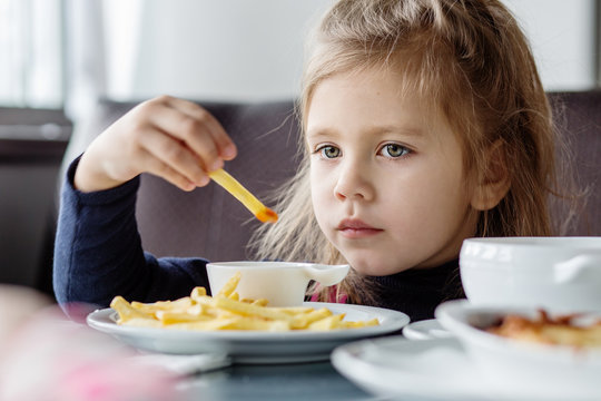 little girl sitting at table and eating French fries