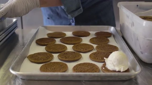 Vanilla ice cream scoops being placed on a cookie sheet filled with cookies to make ice cream sandwiches