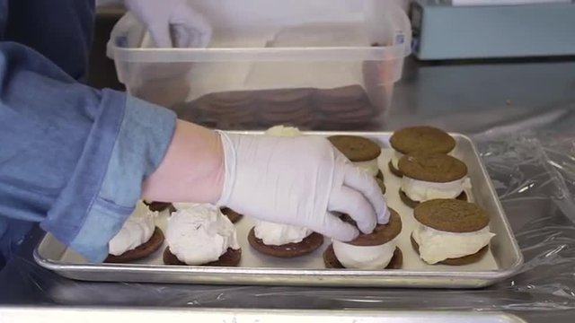 Woman's hand in latex gloves placing cookies ontop of ice cream scoops to make ice cream sandwiches