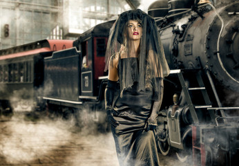 a girl in black on the platform of the railway station in the background of an old-fashioned locomotive