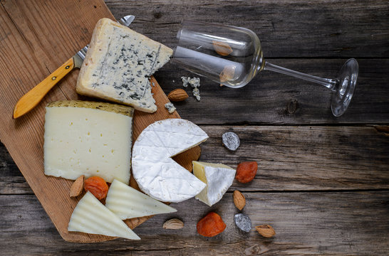Different types of cheese and wine glass on a wooden board