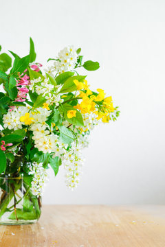 Bouquet of wild spring flowers - rapeseed and european bird cherry - in a jar. Selective focus