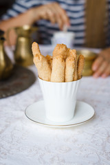 Shortbread biscuits in white cup and woman stirring tea in a cup in the background. Biscuits are...