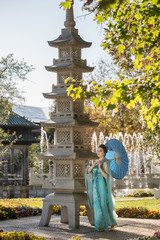 beautiful geisha with a blue umbrella near stone pagoda on background of blur fountain