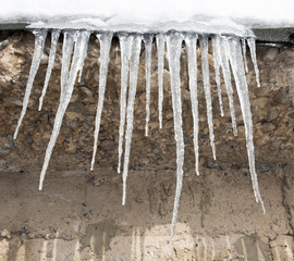 Large icicles hanging on the roof of the house in springtime