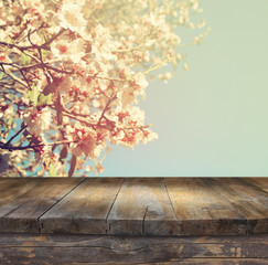 wooden rustic table in front of spring white cherry blossoms tree. vintage filtered image. product display and picnic concept
