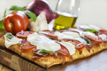 Selective focus was used on this hot, fresh grilled rustic crust pizza topped with Roma tomatoes, fresh mozzarella, Italian salami, basil and red onion.