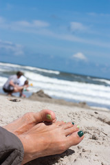 The feet of a woman with green painted nails, in the background you can watch someone the build the sandcastle.