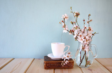 old book, cup of coffee next to spring white flowers on wooden texture
