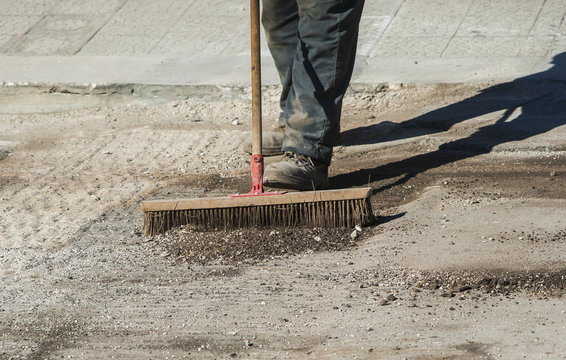 worker with large scrub brush collect residues of asphalt milling