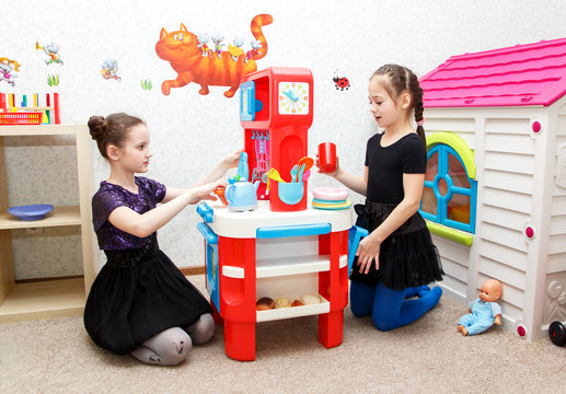 Two little girls play role game with toy kitchen in day care