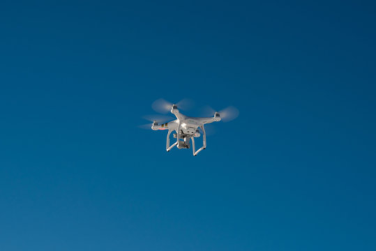 White drone quad copter with flying in the blue sky 
