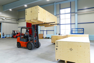 Gabelstapler in einer Halle hebt schwere Holzkiste mit Bauteilen der Maschinenindustrie