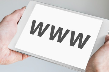 WWW (world wide web) text displayed on touch screen of modern tablet. Hands holding white mobile...