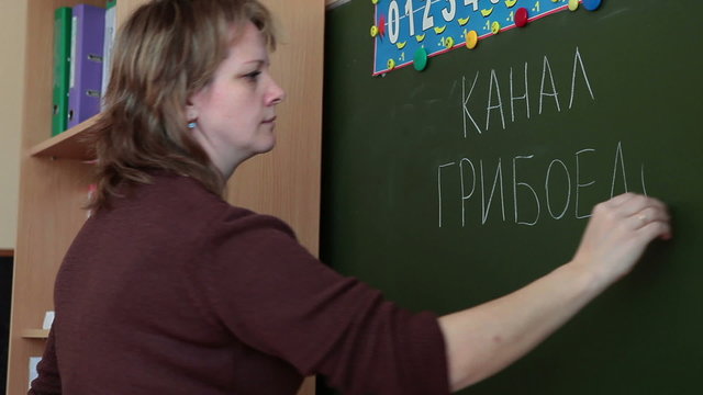 Woman teacher writes on the green blackboard the words