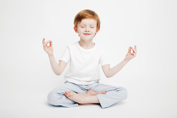 Little cute red-haired boy sitting on a white background in the