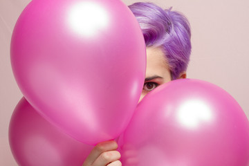 Violet short-haired girl in pink pastel peeking behind balloons