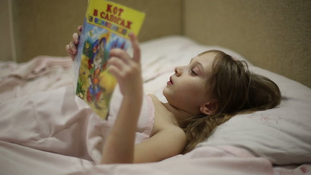 The girl is reading the book bedtime, she is lying on the bed

