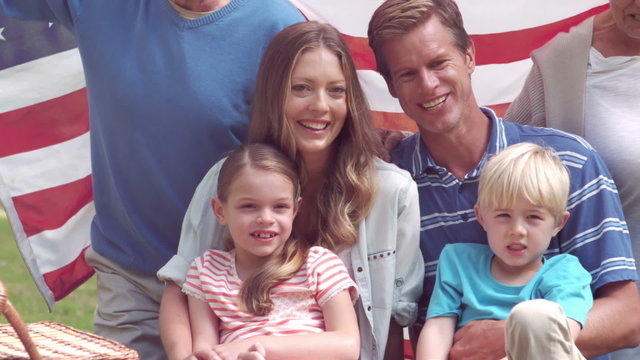  Happy family smiling with an american flag in a park