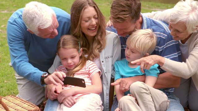  Happy family smiling using smartphone in a park