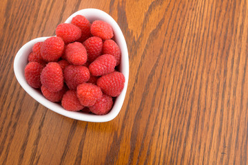 Close-up of fresh red raspberries in a white heart shaped bowl
